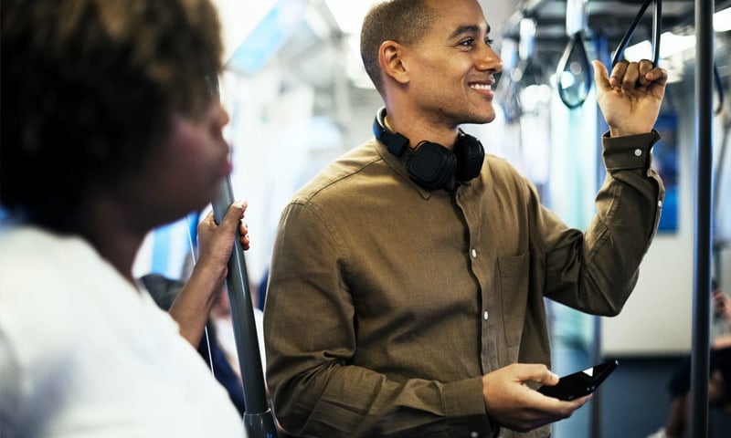 Man smiling while holding a phone on a crowded train.