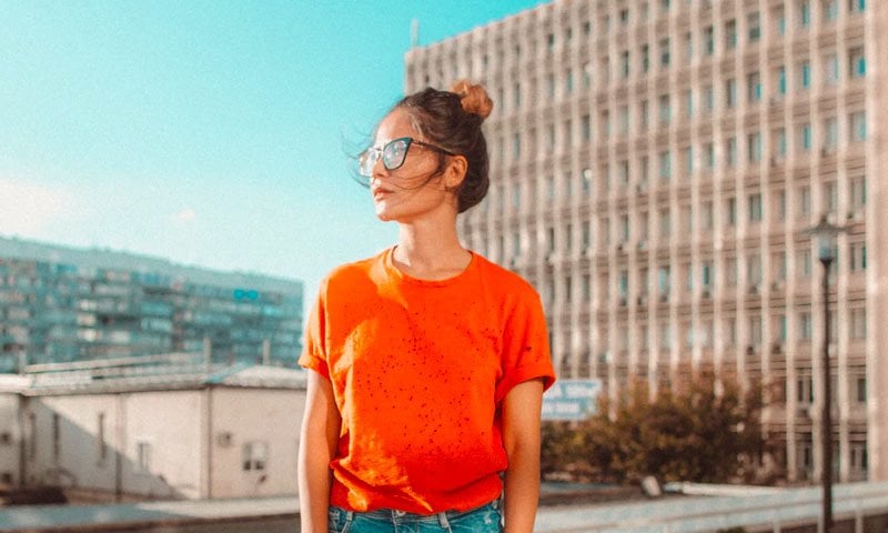 Woman in bright orange shirt wearing glasses stands outdoors.